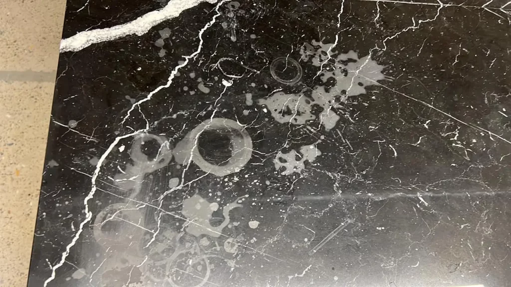 Dull etch marks on a polished black marble surface